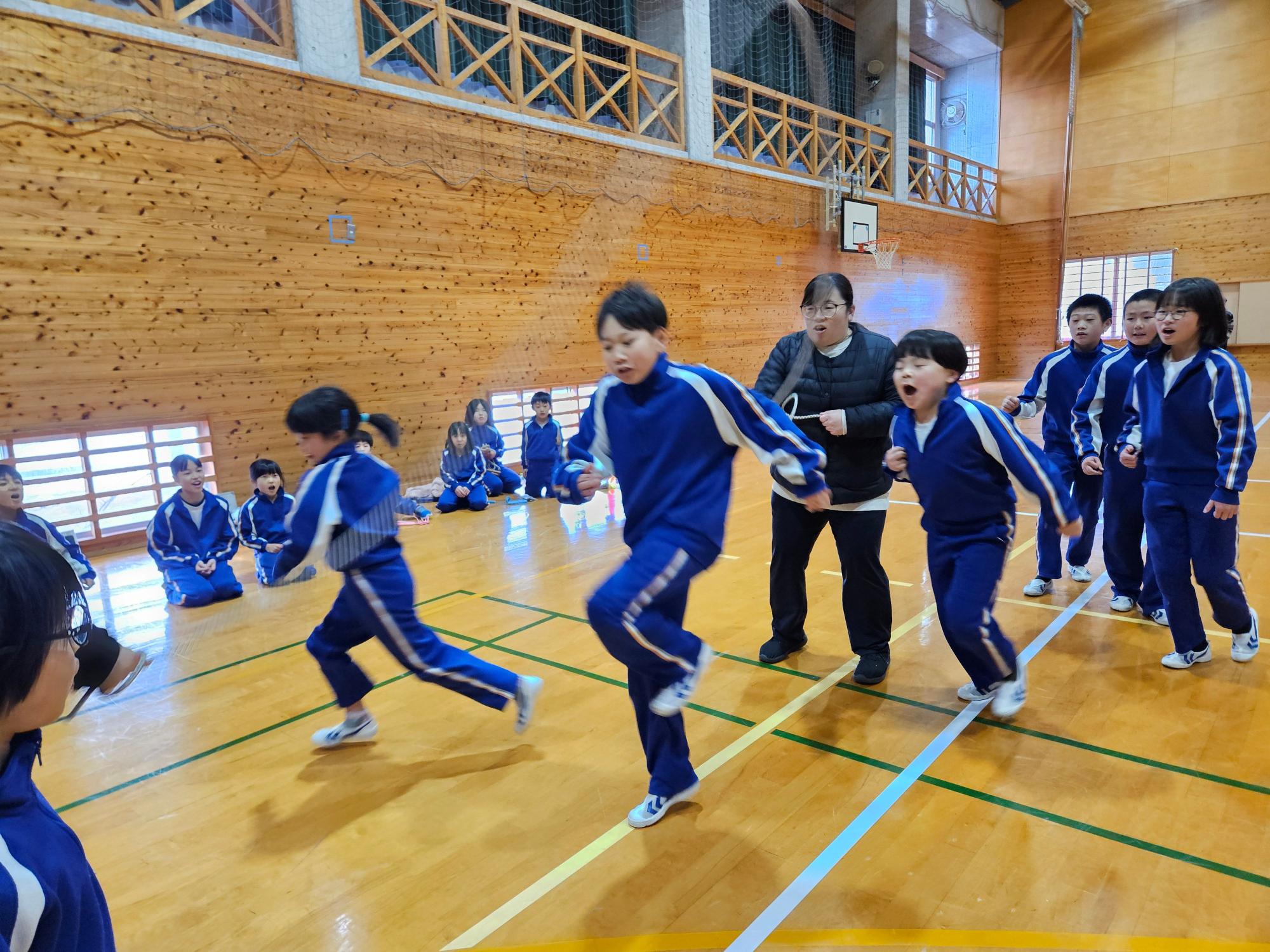体育館で青色のジャージを着た児童たちがリレーをしている写真
