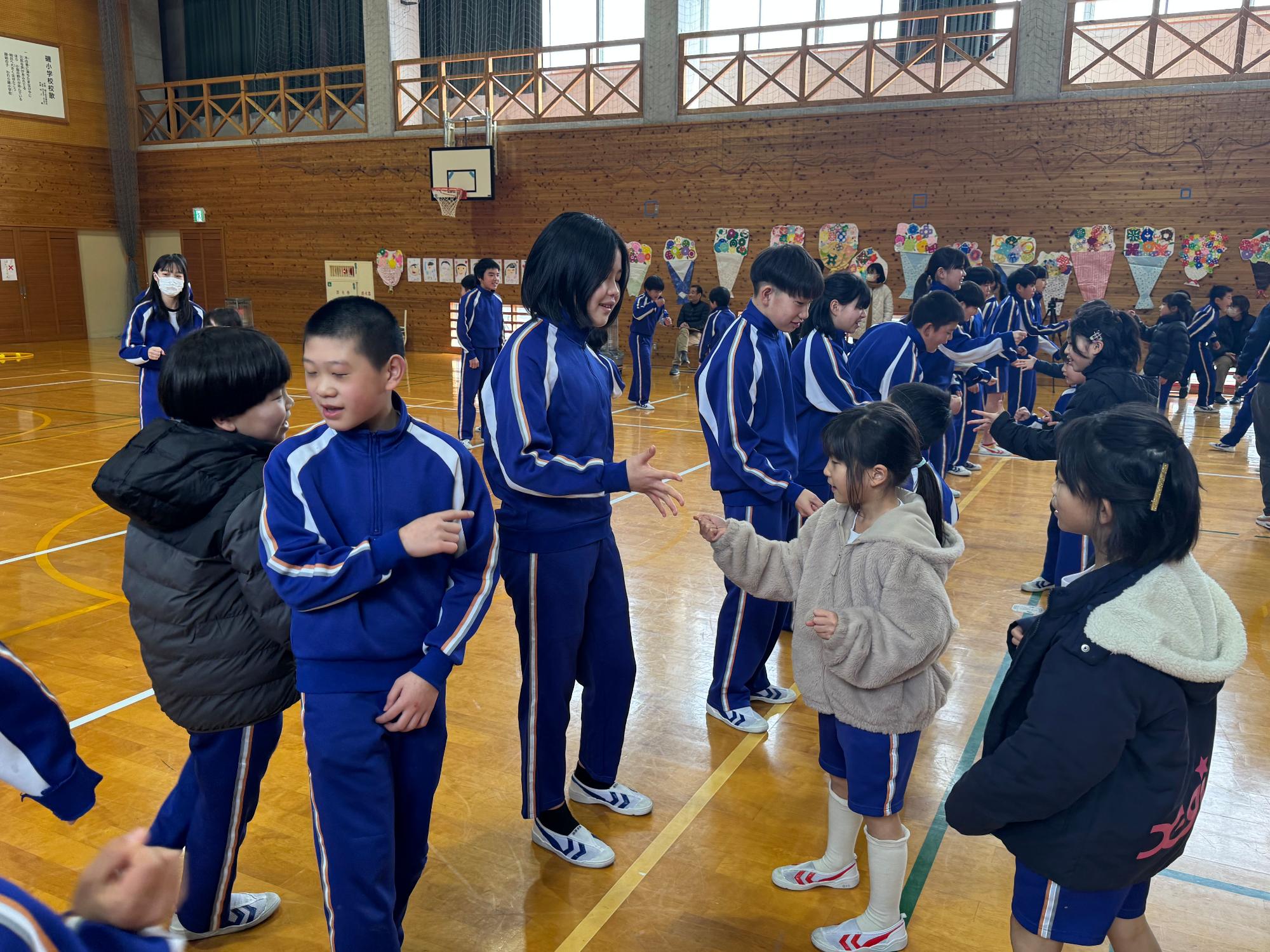 体育館で青色のジャージを着た児童たちがじゃんけんをして交流している写真