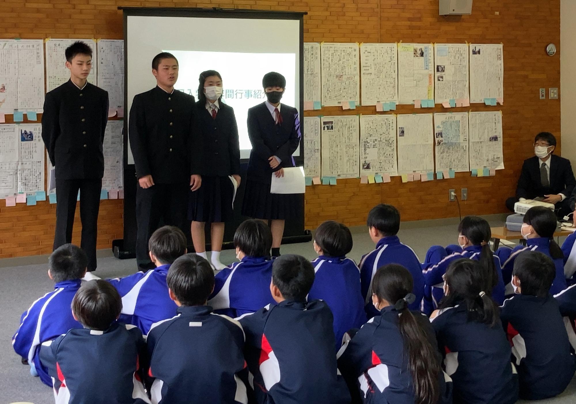 教室に座っている生徒たちの前でスクリーンを使用して制服姿の生徒たちが説明している写真