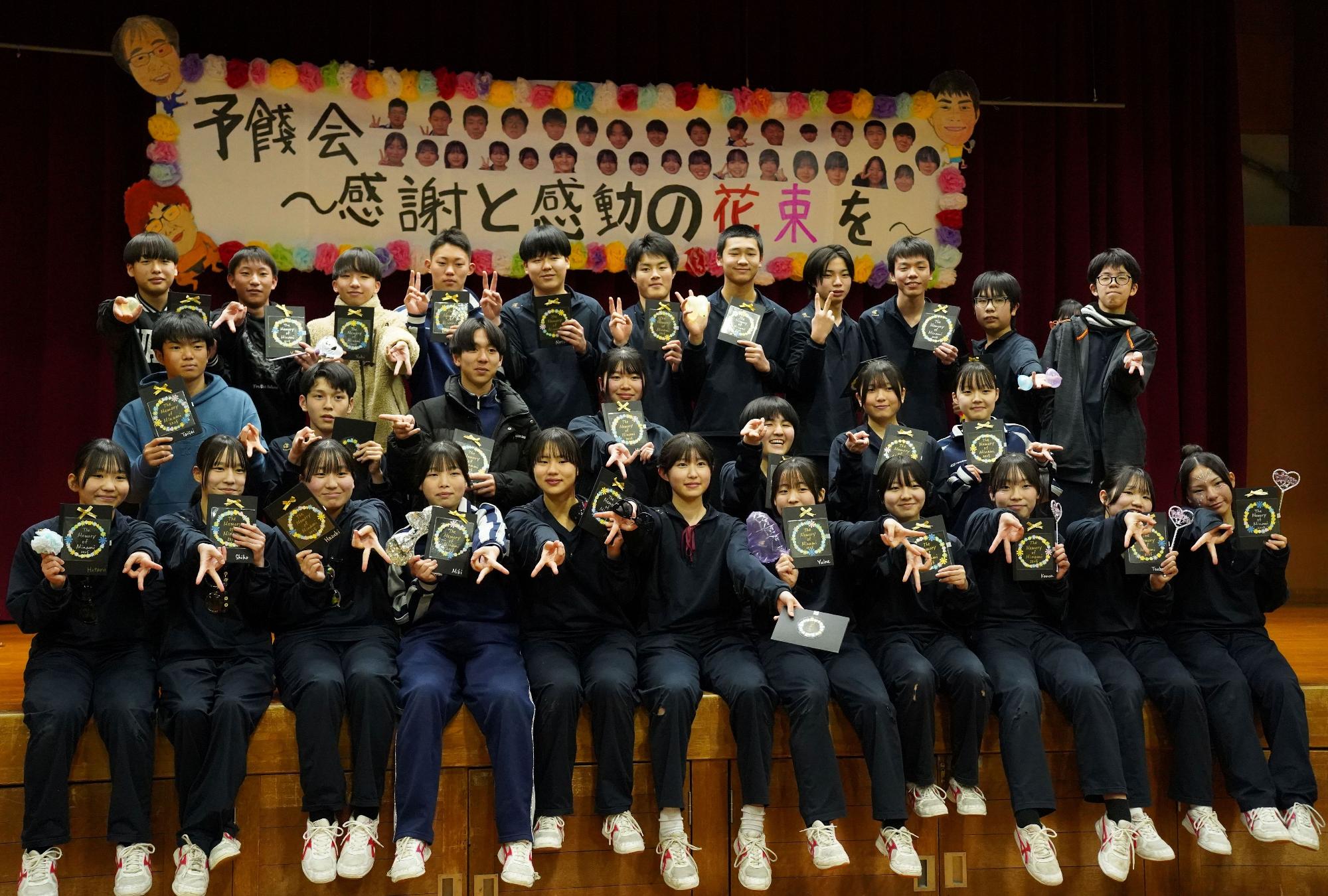 舞台上でユニフォーム姿の生徒たちが記念撮影をしている写真