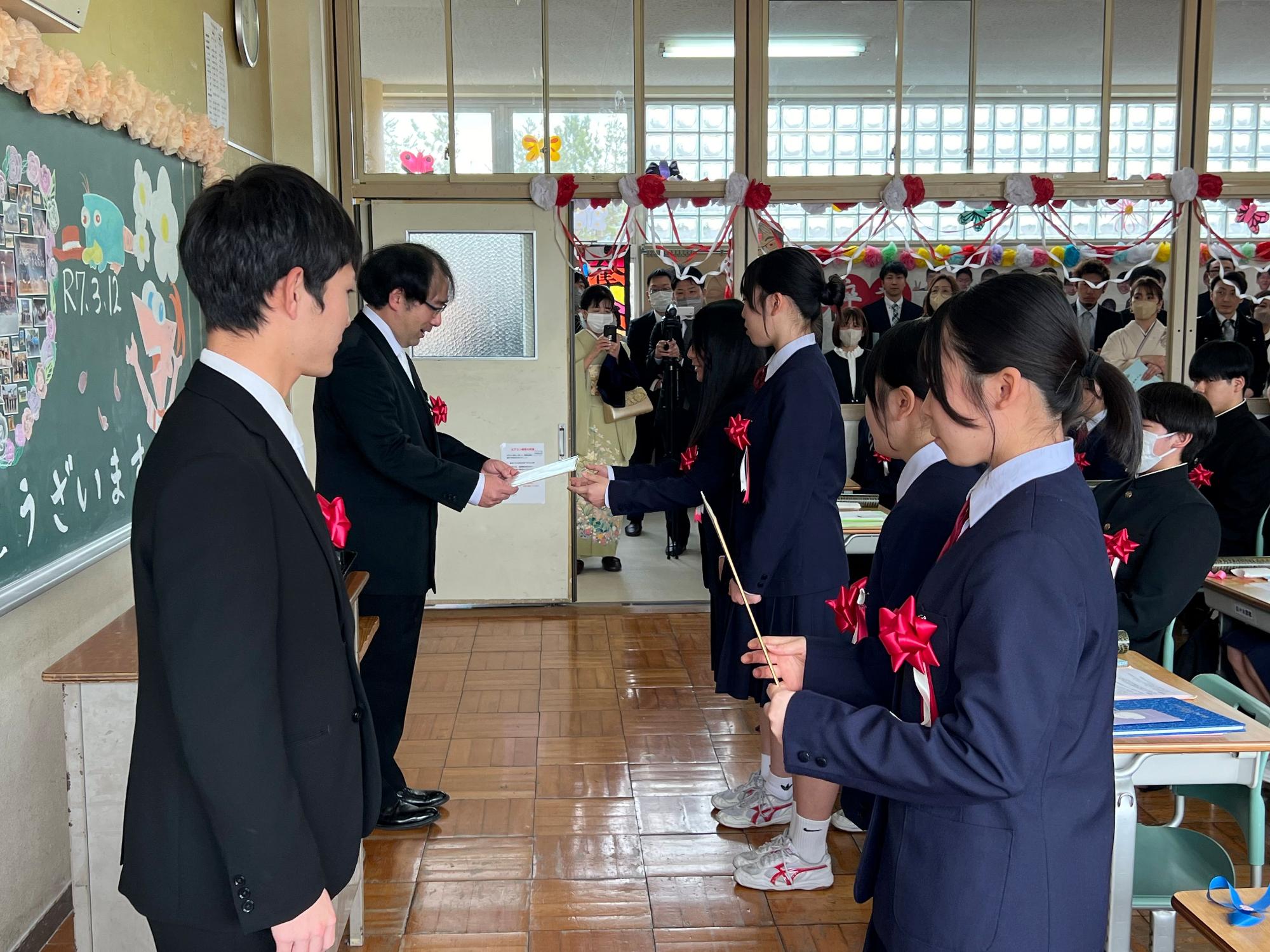 教室で女子生徒が先生から証書を受け取っている写真