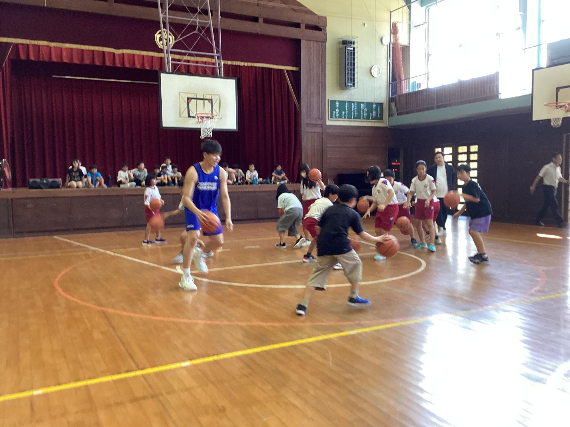 体育館で体育着を着た生徒たちがバスケットボールの試合をしている写真