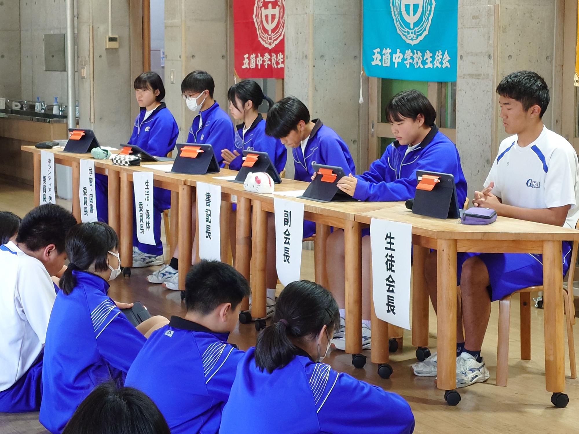 生徒会役員が横並びで着席しタブレットを使いながら会議を行っている写真