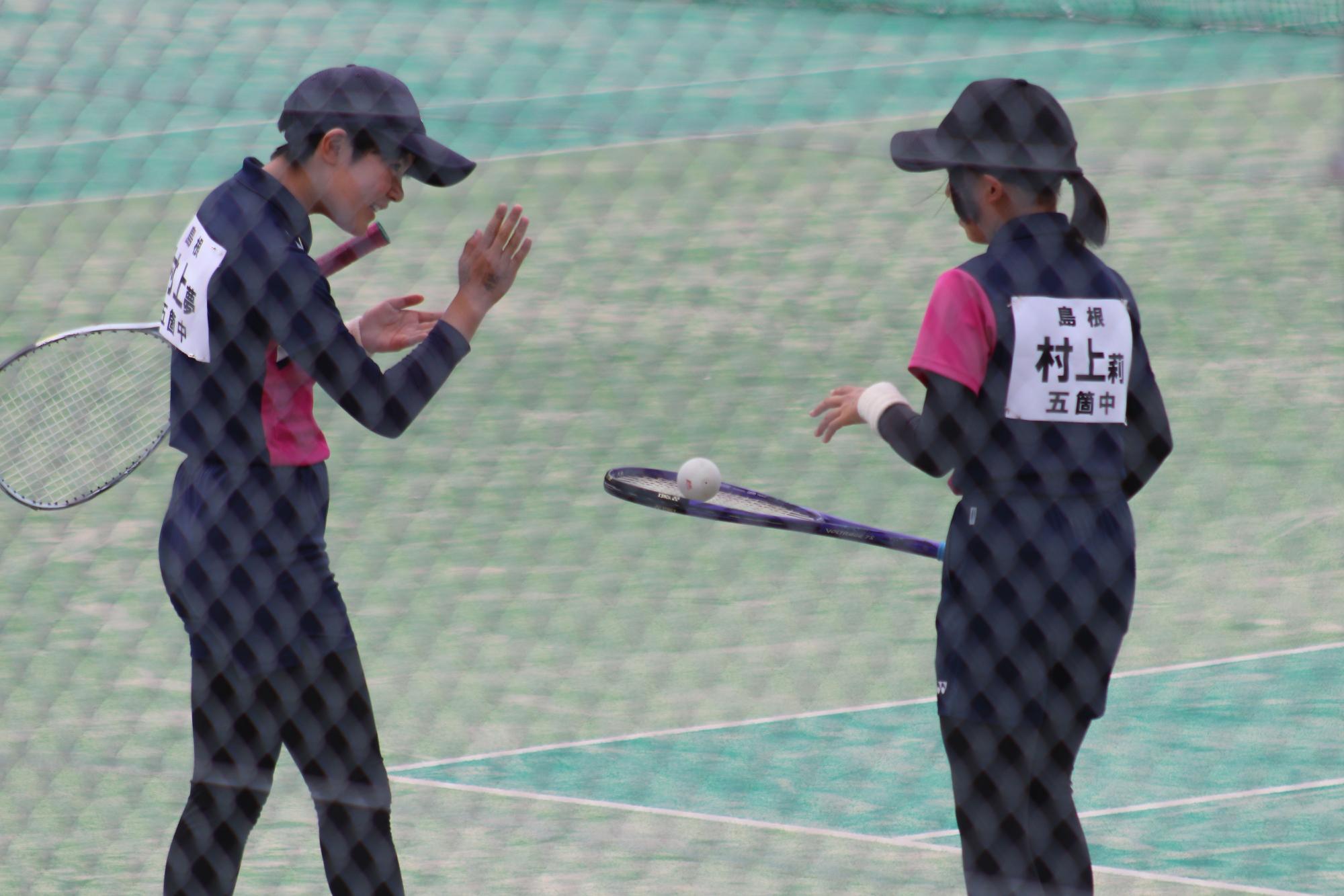 テニスコートで選手二名が試合中に声を掛け合っている写真
