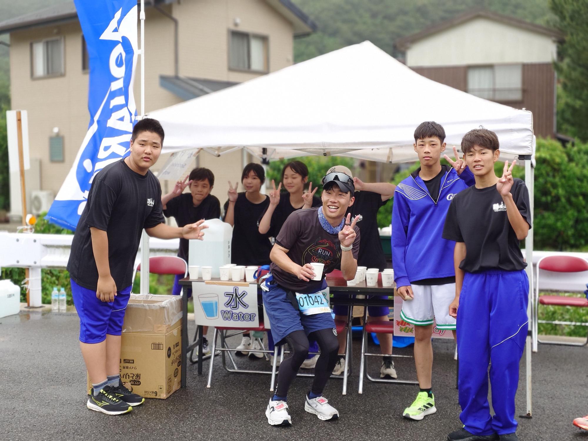 給水所を備えたテントの前で生徒たちが記念撮影をしている写真