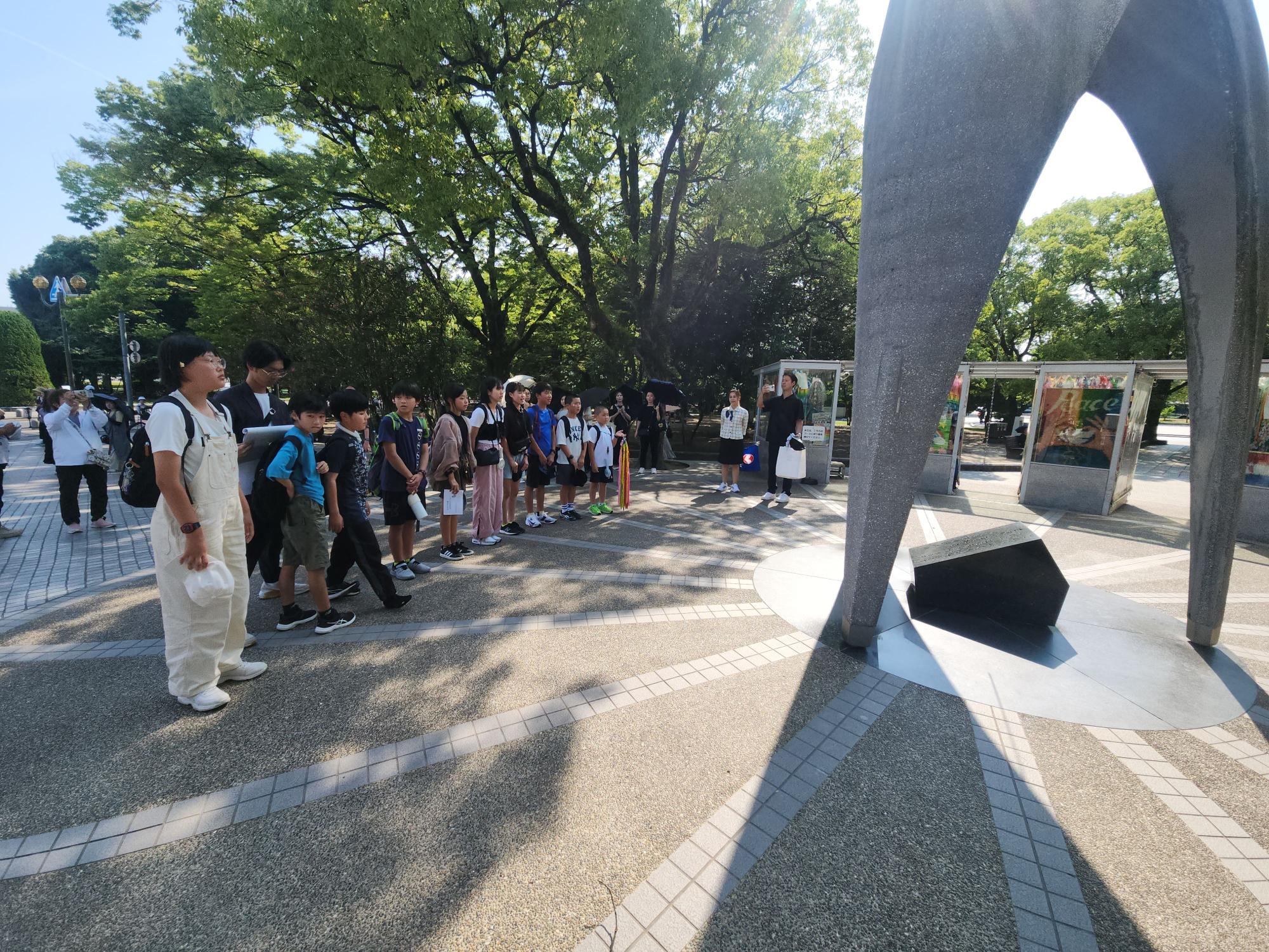 児童たちが屋外で記念碑の見学をしている写真