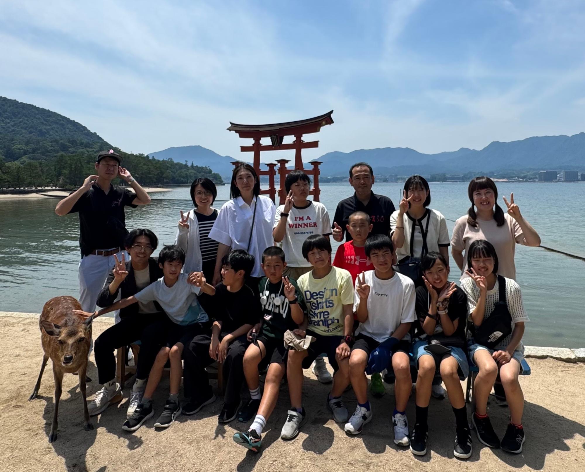 鳥居のある海辺を背景に児童と引率者が記念撮影をしている写真