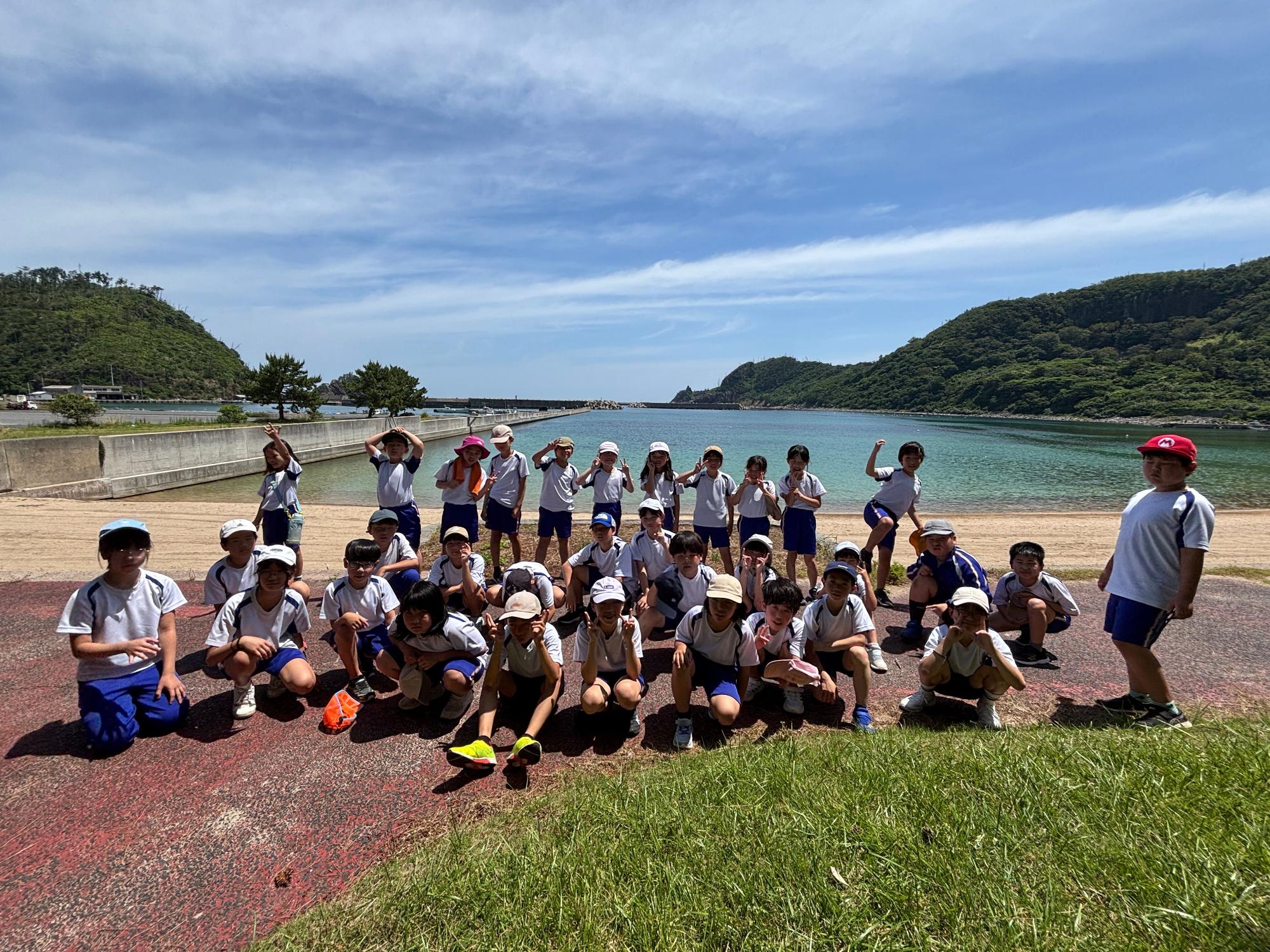 海辺で児童たちが青空の下、記念撮影をしている写真
