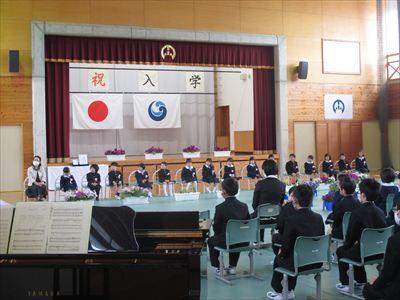 体育館の前方に新入生が一列に並び入学式が行われている写真