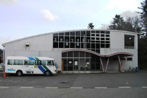 入口の波打った形の屋根が特徴的で、手前に白いボディに青のラインが入ったバスが停まっているスポーツクラブ隠岐の写真