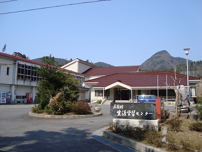 奥に山が見え、手前に円形状のロータリーがある赤い屋根の隠岐の島町立五箇生涯学習センターの写真