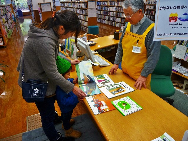 色々な絵本を読んでいる親子とそれを見守っている男性職員の写真