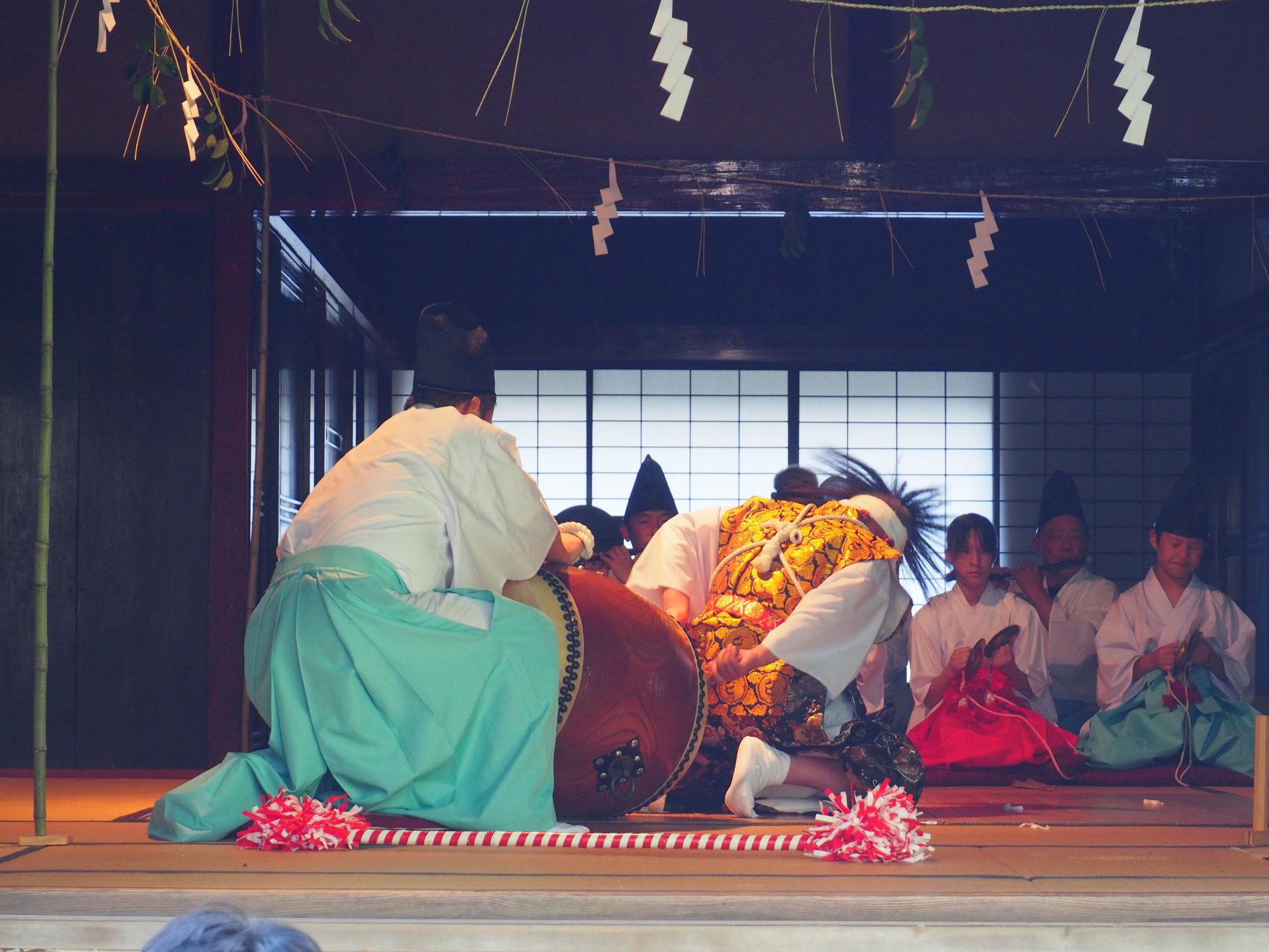 神楽公演の写真。はやし方の前で2人の男性が神楽を舞っている。