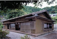 森を背景にした、石置き屋根の佐々木家住宅の写真