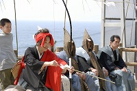 黒と赤の服装の役主が弓に矢をつがえている様子の長尾田百手祭風流の写真