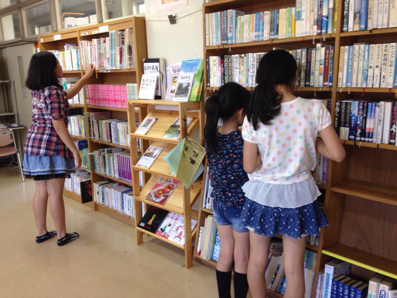 図書館で本を選んでいる女子児童3人の写真