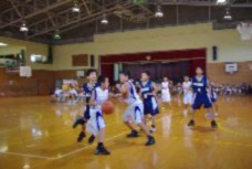 学校ごとのユニフォームをを着てバスケットボールをしている児童たちの写真