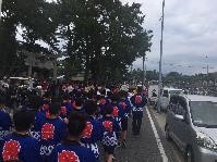 児童たちが「祭」と書いたお揃いの法被を着て歩道を歩いている写真