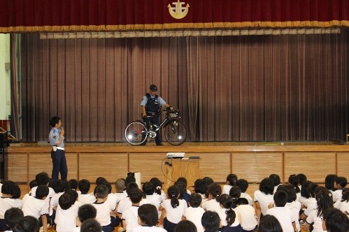 体育館で警察署の方の自転車についての説明を聞いている児童たちの写真