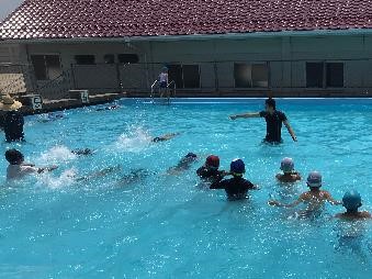 プールの中で水着の児童たちが水泳の授業を受けている写真