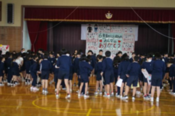 体育館の手作りの飾りつけで装飾されたステージ前に集まっている児童たちの画像