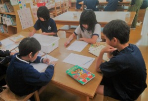 机を囲んで児童たちが座り、それぞれ紙に向かって書いたり考えたりしている写真