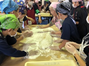 エプロンと三角巾をつけた多数の児童が、テーブルに広げた餅を丸めている写真