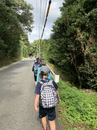 道路をリュックを背負った児童たちが1列で歩いている写真