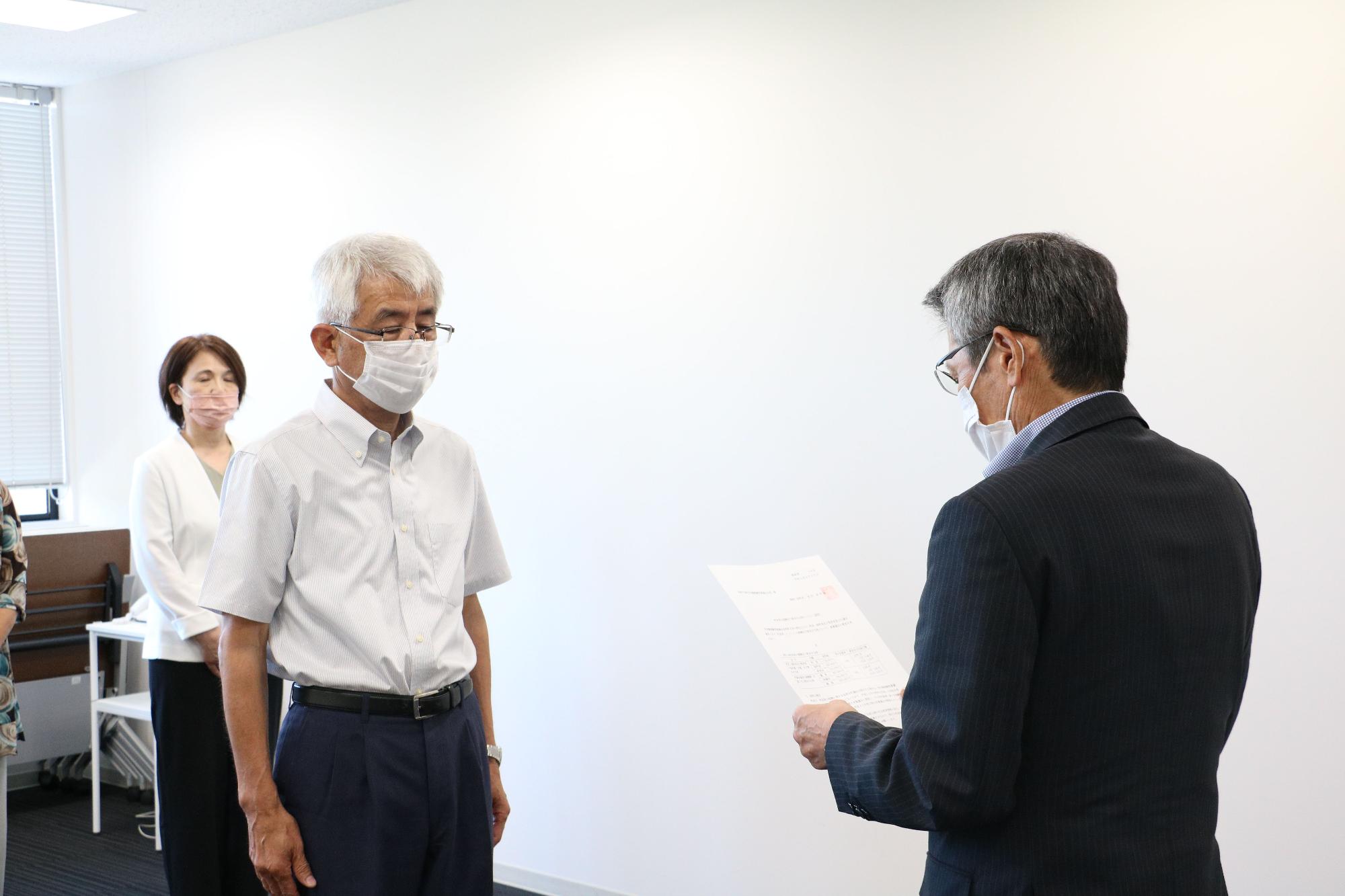 書面を両手に持っている男性とその前でもう一人の男性が向かい合っている写真