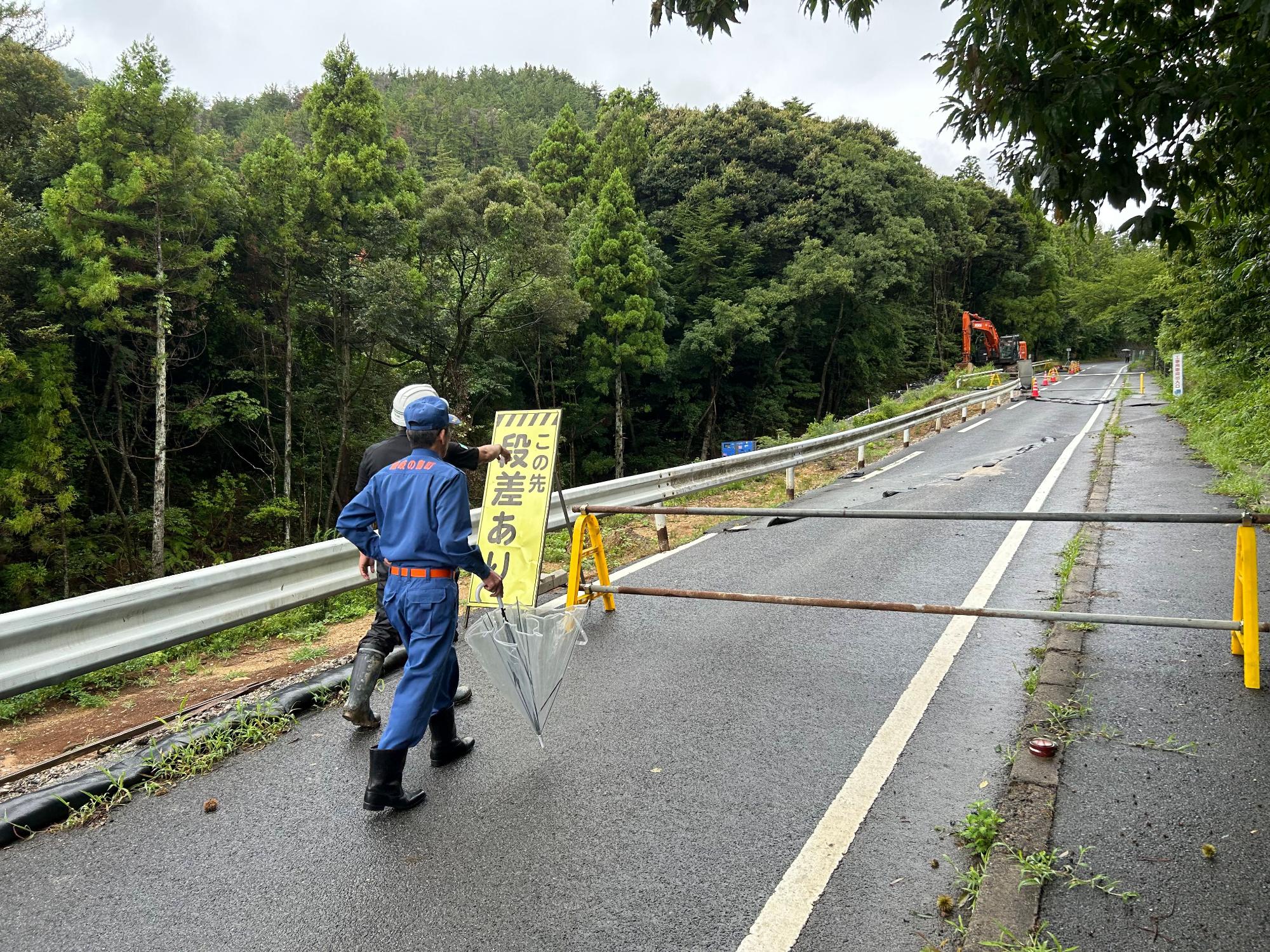 通行止めがされている道路を作業服を着た男性二人が歩いている写真