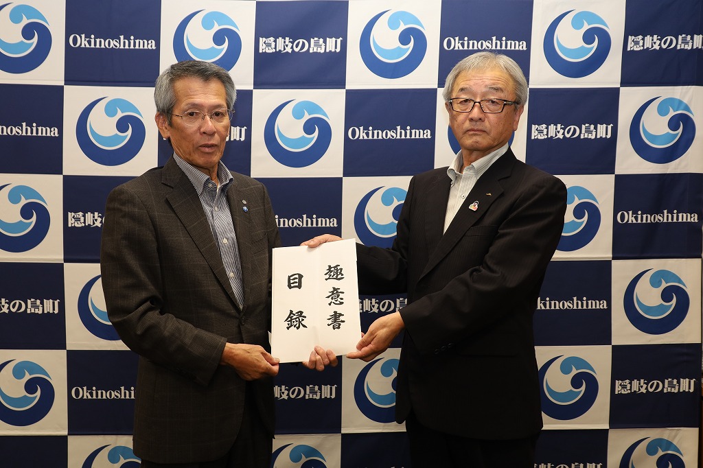 「趣意書 目録」と書かれた書面を男性二人が共に手に持っている写真