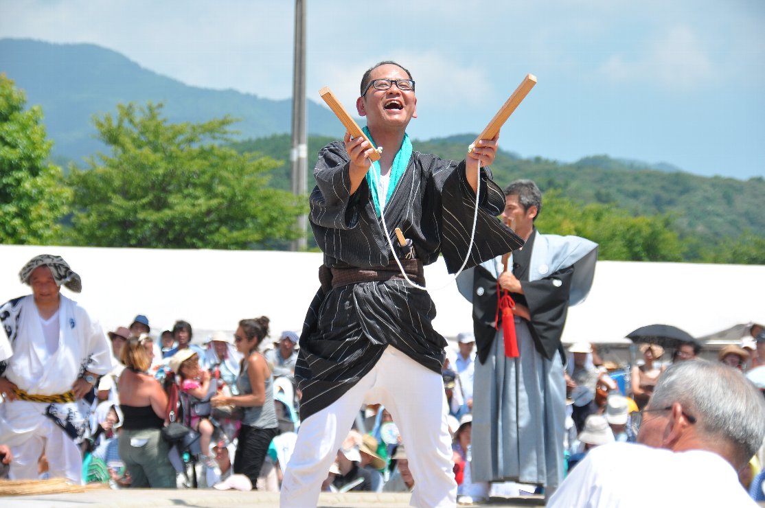 黒の上着を着た男性が紐でつながった木の棒を持っている写真