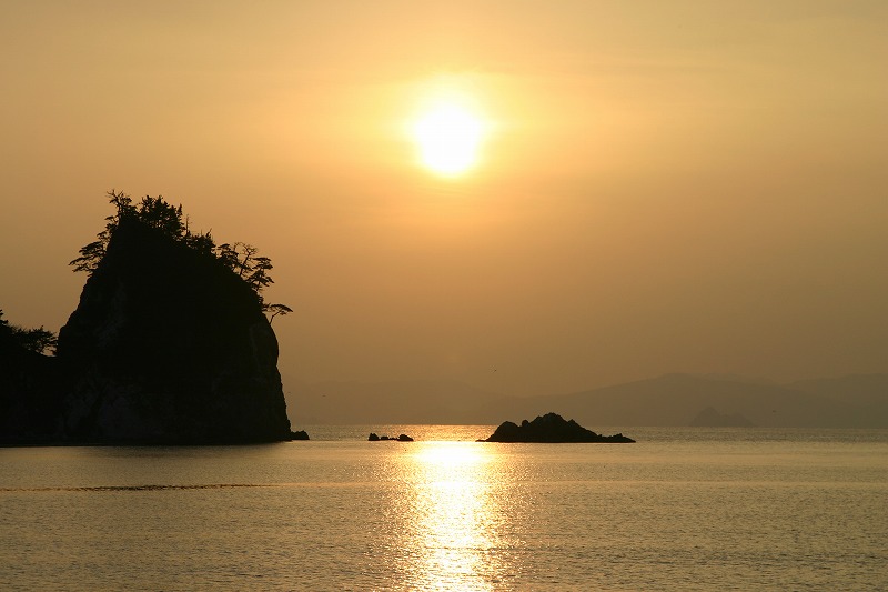 夕日に照らされた海面と岩場の写真