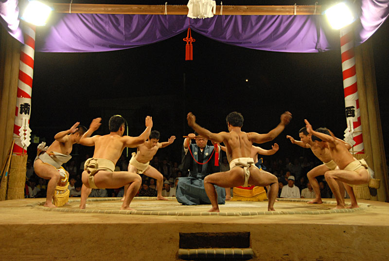 土俵際で行司を囲むように並んだ力士たちが手を上げている写真