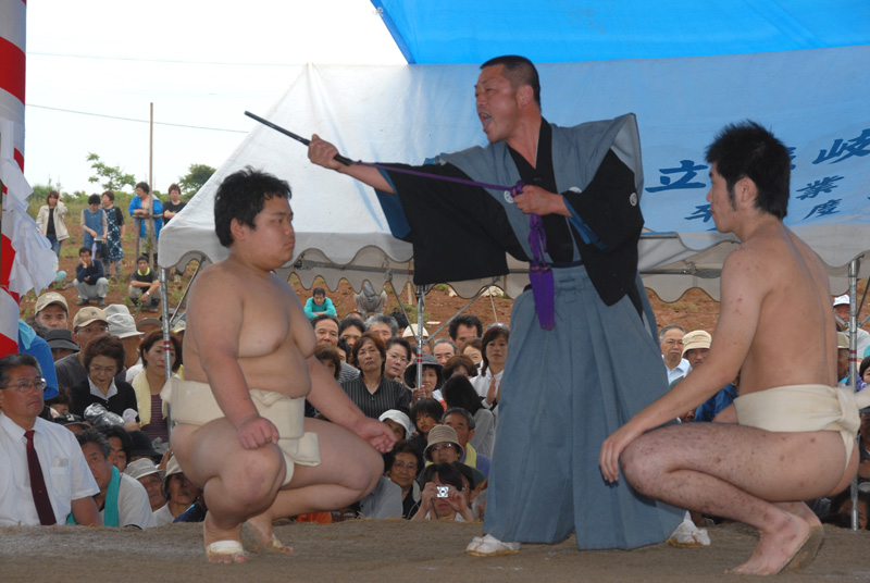 行司が向かって左側の力士に棒を突き出している写真