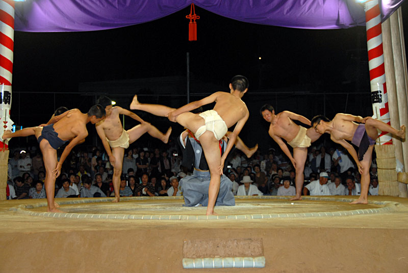 行司が中央にいる土俵で力士たちが片足をあげている写真