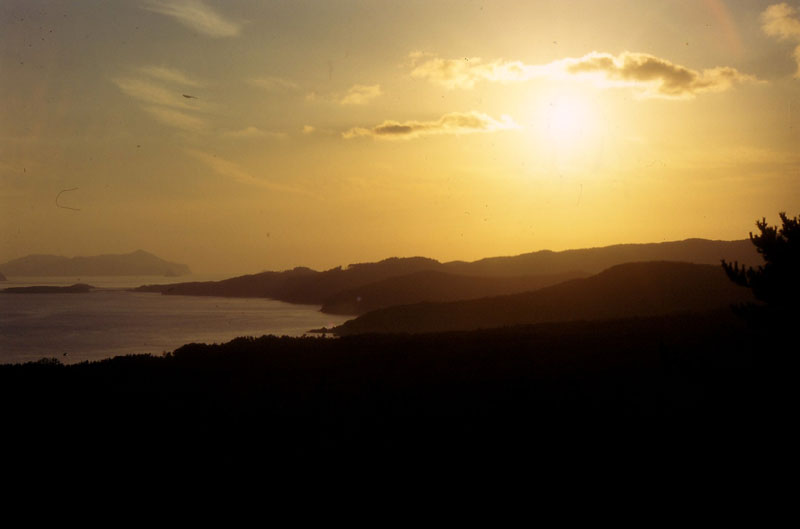 夕日に照らされて暗くなっている海と山の写真