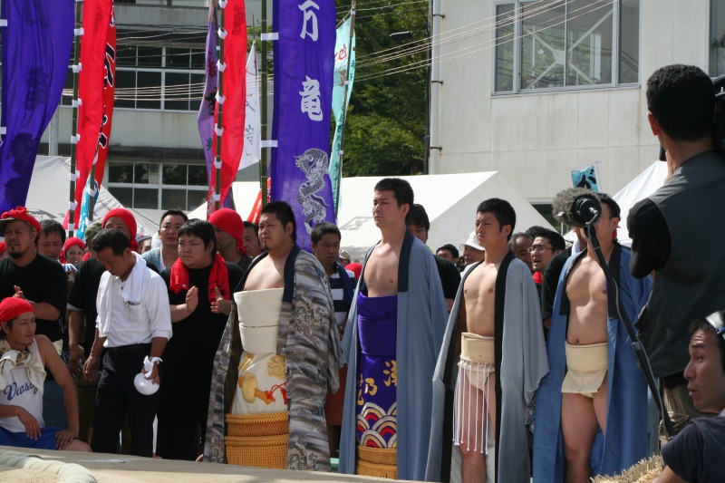 土俵のそばに上着を羽織った力士たちが並んでいる写真