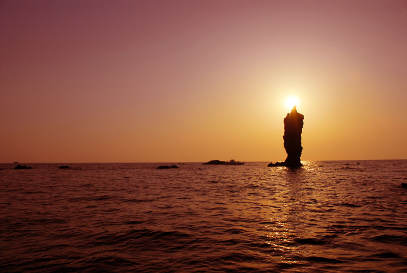 海から突き出た岩が朝日と重なっている写真