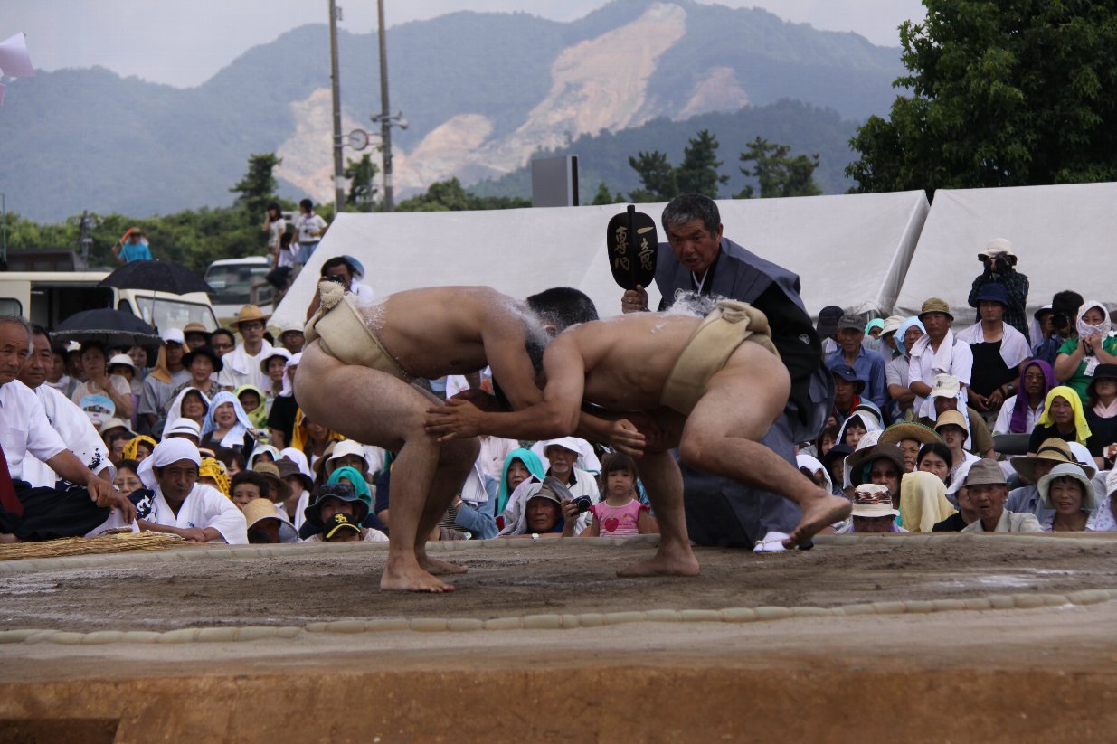軍配扇子を立てて2人の力士を見ている行司の写真