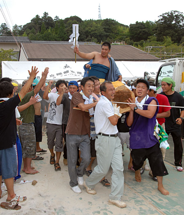 丸太に乗った力士を大勢の男性が担いでいる写真
