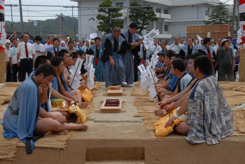 たくさんの力士が土俵の上で向かい合って並んで座っている写真