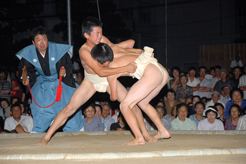 暗くなった野外の土俵で子ども二人が相撲の試合をしている写真