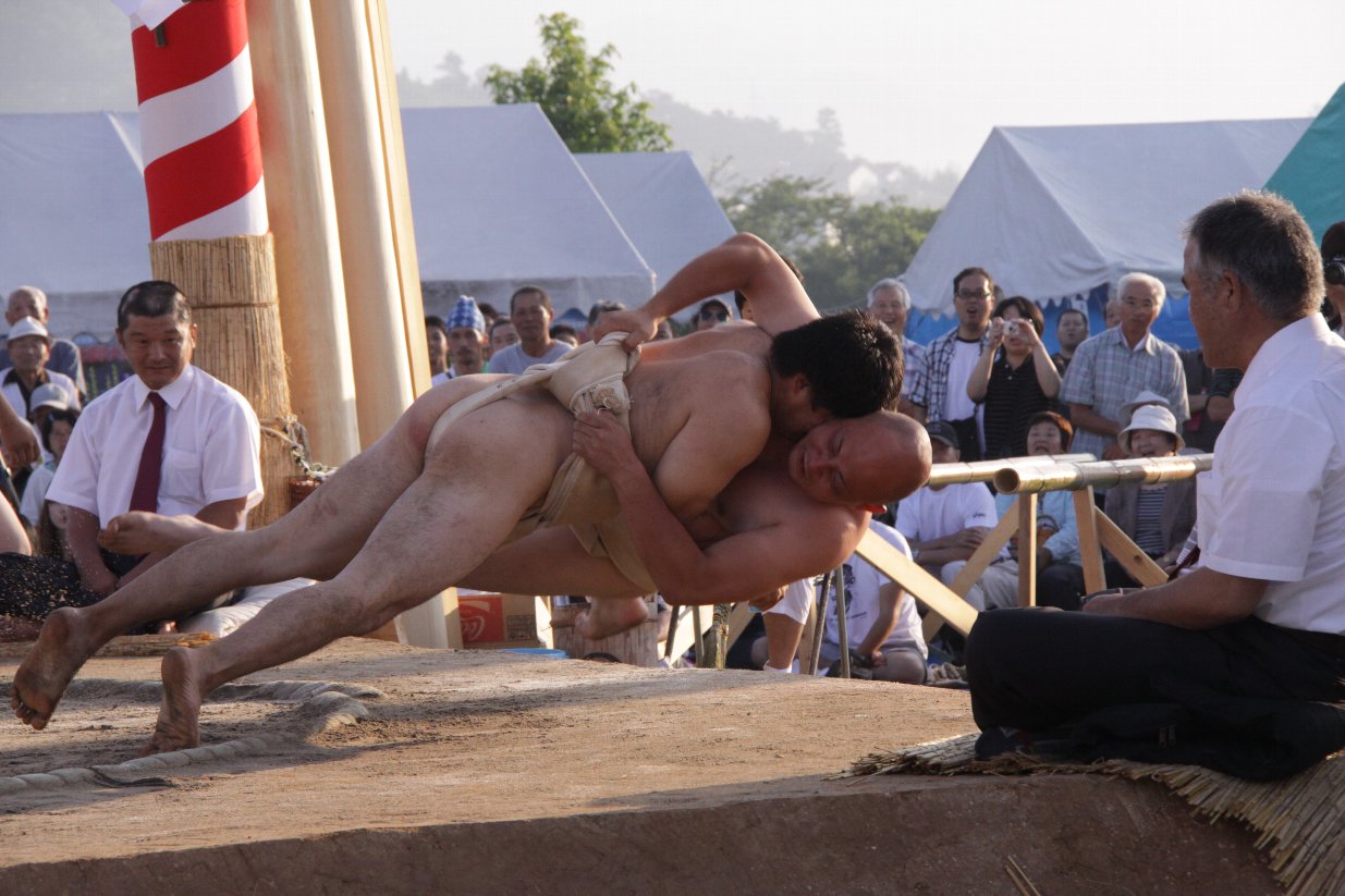 2人の力士が土俵外へ倒れ込もうとしている写真