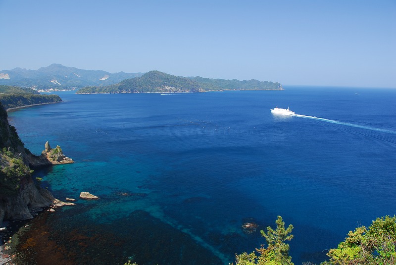 透き通った青色をした海の上を船が進んでいる写真