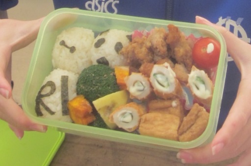 両手で弁当箱を持ち、中にはおにぎりやおかずがきれいに詰められている写真