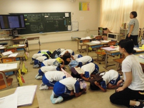 児童たちが教室の床にしゃがみ込み、持ち物で守る頭を訓練をしている写真