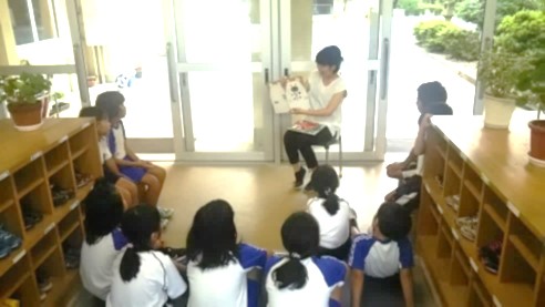 学校の昇降口に児童が集まり先生の読み聞かせを聞いている写真