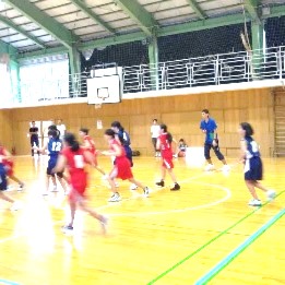 学校ごとのユニホームを着てバスケットボールの試合をする児童たちの写真