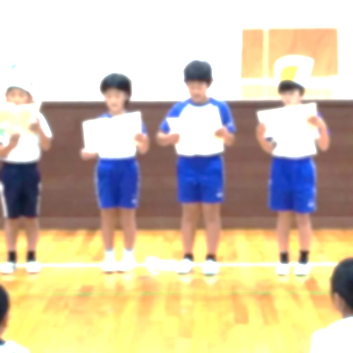 全校児童の前で紙を見ながら音読発表をする児童たちの写真